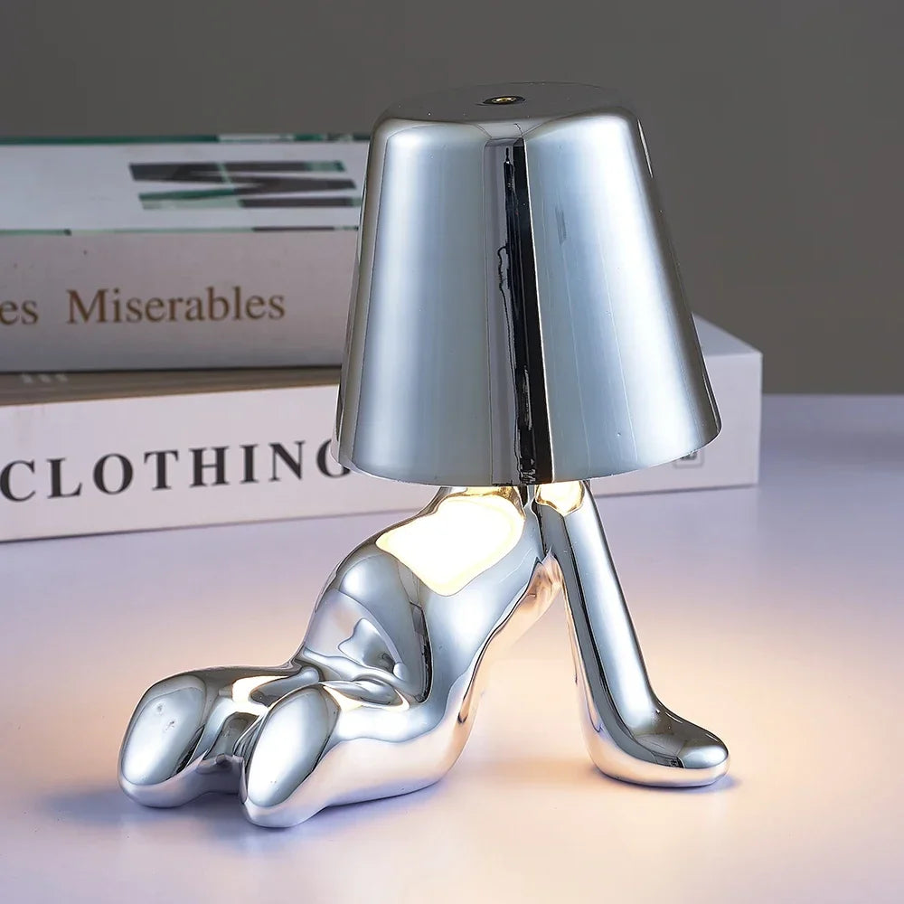 Designerska lampa stołowa LED — figurka w pozycji siedzącej, połyskujące wykończenie | Norivo Norivo